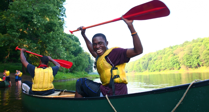两个年轻人穿着救生衣坐在独木舟,向空中举起桨在明显的庆祝活动。其中一个对着镜头微笑。