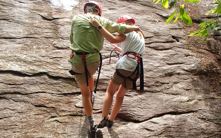 父母和孩子互相用双臂环绕着垂降岩墙。都是穿着安全装置,获得了绳索。